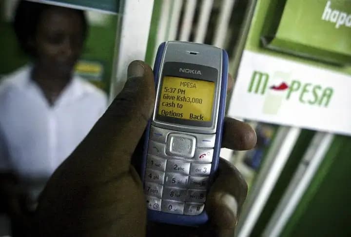 A user holding a dumb phone with an SMS of a bank transfer